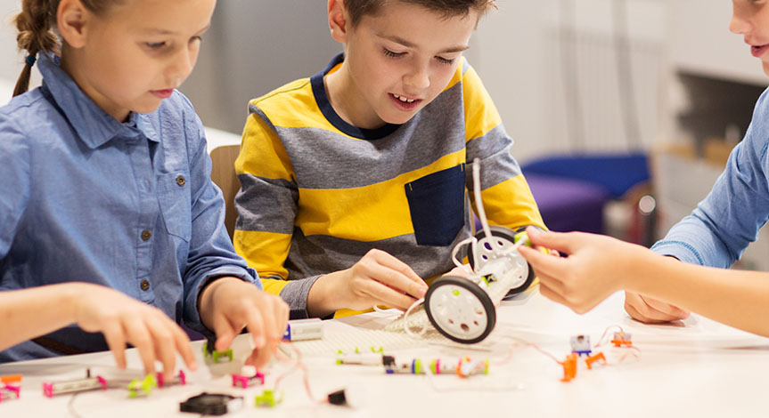 2 boys and a girl building a robotic vehicle on the table