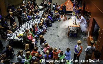 Mad scientist performing on a table with smoke, beakers, in front of children