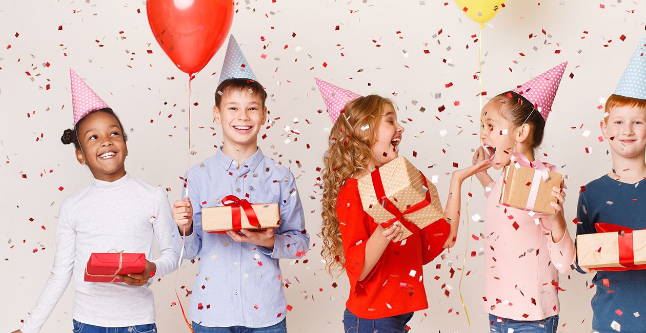 Kids celebrating birthday holding balloons and presents wearing birthday hats with confetti falling over white background