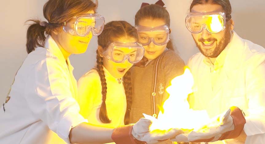 Kids and mad scientists wearing safety goggles looking at paper on fire