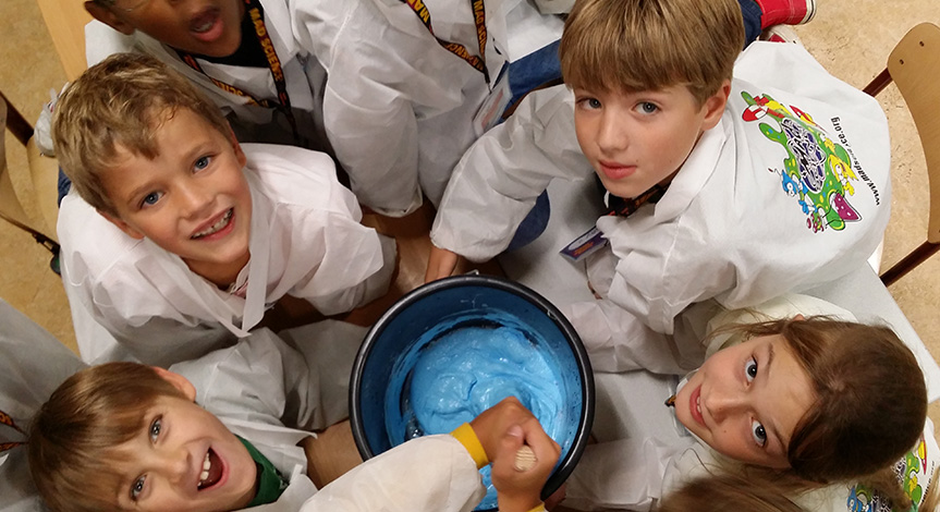 Kids looking up while mixing a big bucket of blue slime